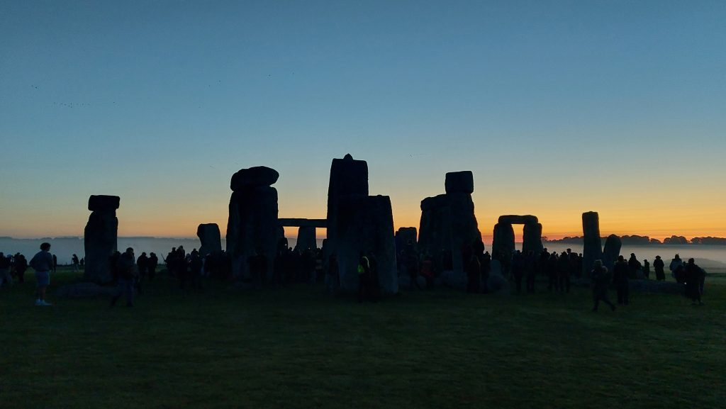 Silhouetted by the pre-dawn sky, people gather amonst the monoliths of Stonehenge, September 2023