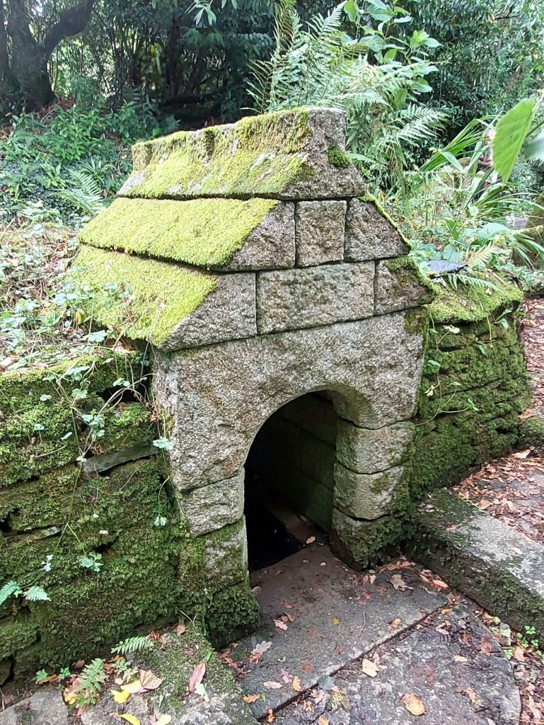 St Keyne's Holy Well, is housed in a simple granite-block shelter set into a bank. The bank walls and the roof of the well house are green and mossy, and ferns grow around it.