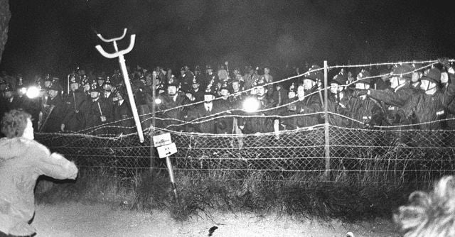 Ranks of riot police stand behind a barbed wire fence around Stonehenge, late 1980s